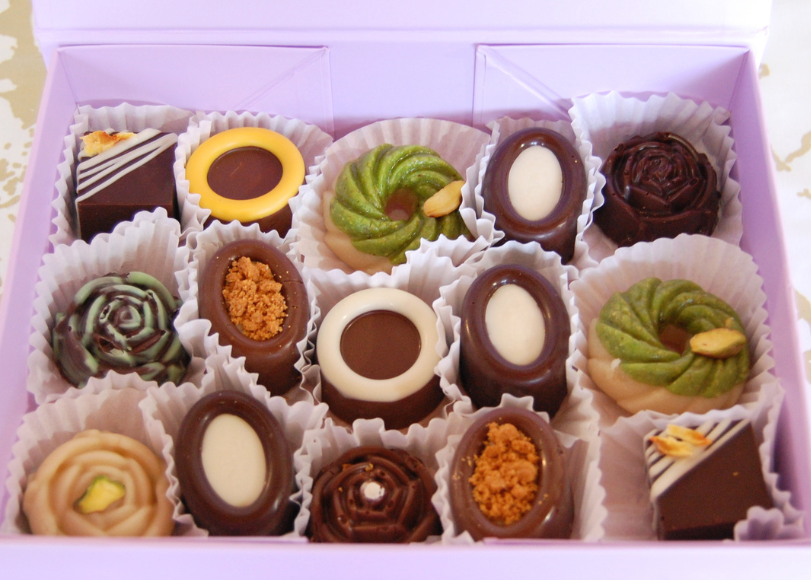 A lavender gift box filled with assorted chocolates and sweets, photographed from above on a light marble-patterned surface.