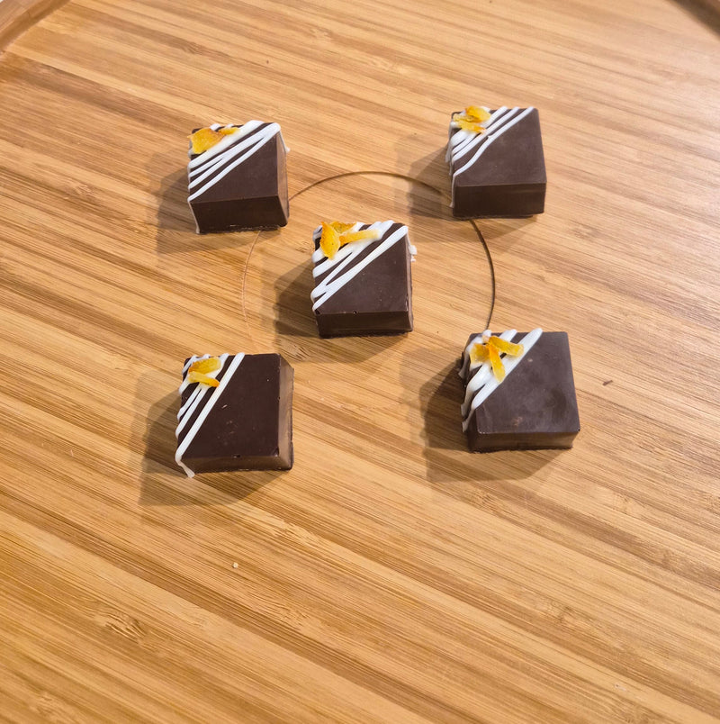 Five chocolate-covered square bars arranged on a light wood surface, each decorated with diagonal white stripes and a yellow star motif.