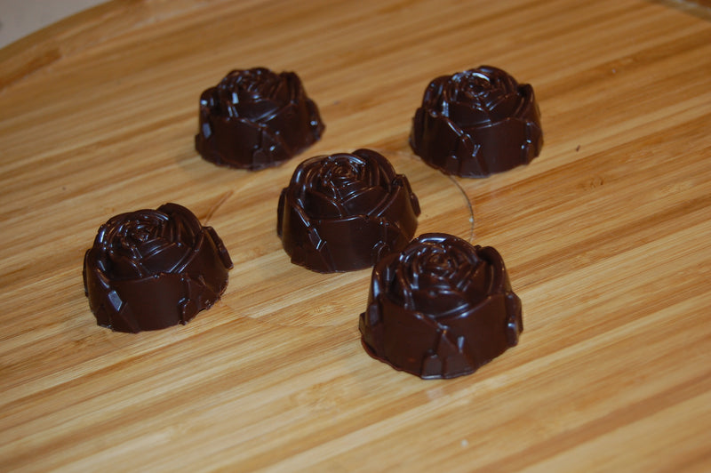 Five chocolate roses with glossy dark chocolate coating arranged on a light wood surface.